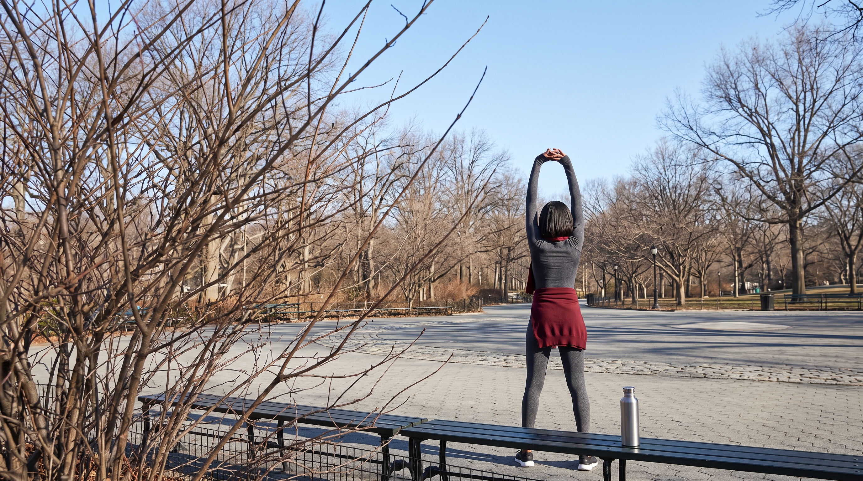 Person stretching arms overhead beside an open window at sunrise
