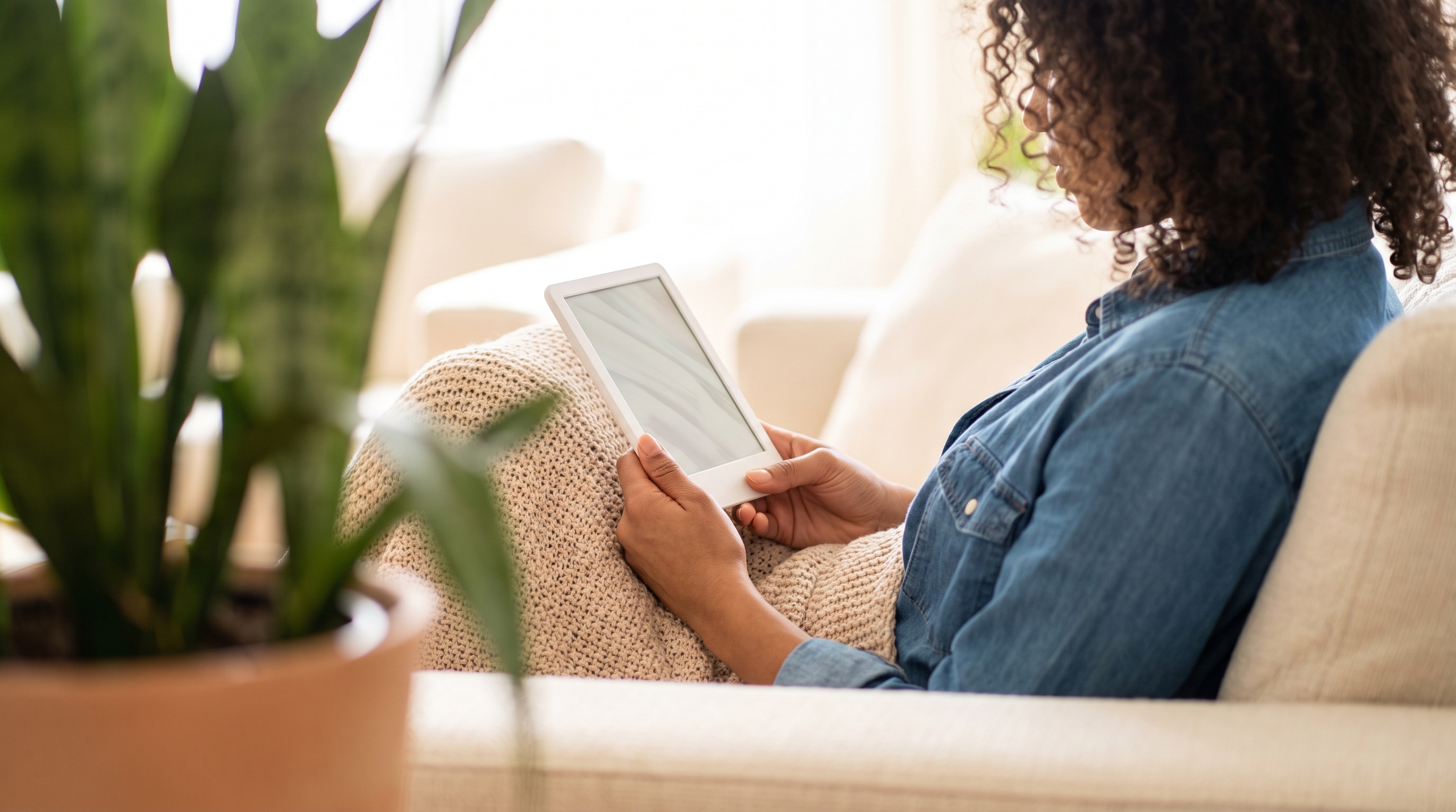 A woman in her 30s reading on the sofa under a blanket