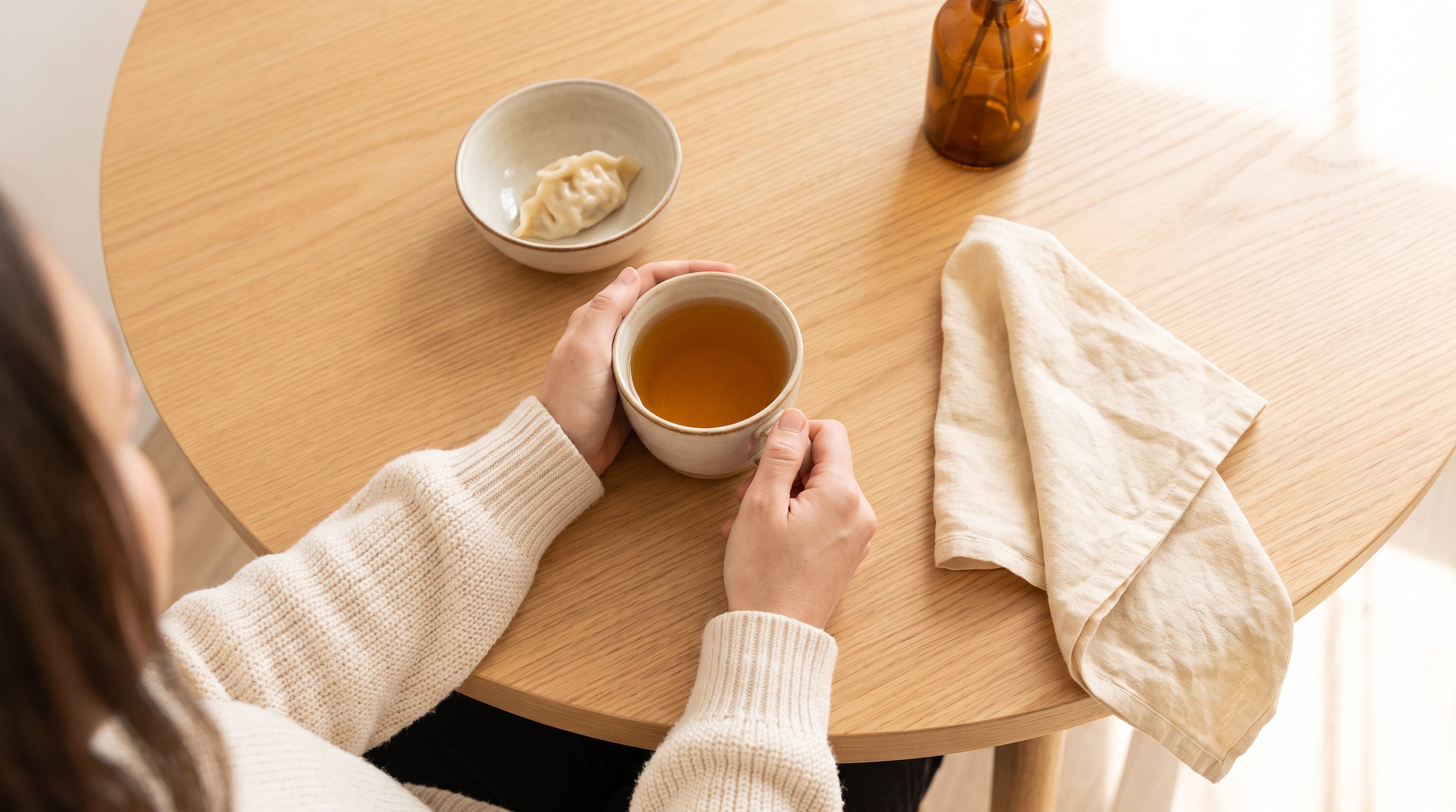 A woman in her 30s sitting calmly at a cozy wooden dining table with a cup of tea