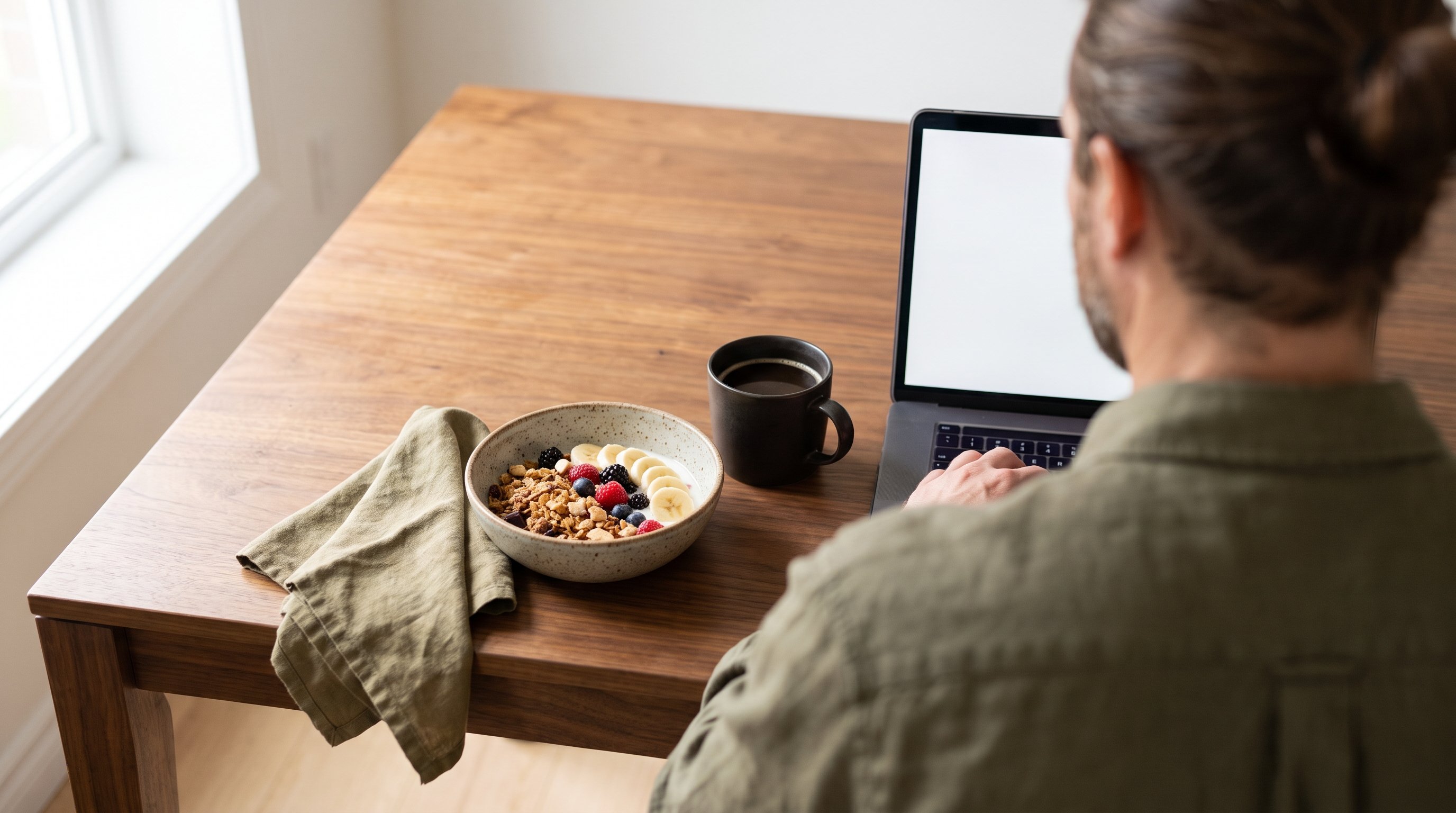 A man in his 30s working focused at a laptop on a kitchen table