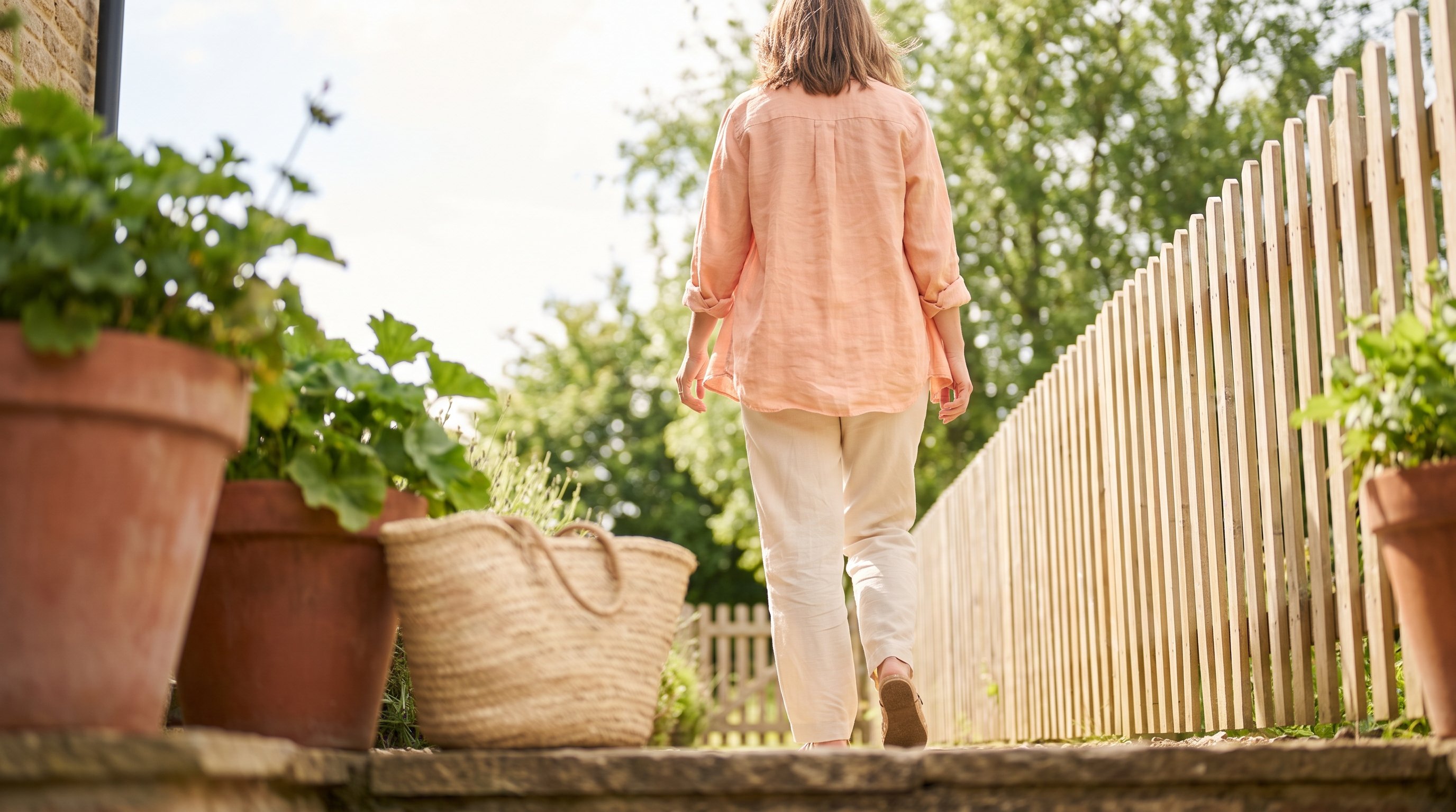 A relaxed woman in her 40s walking outdoors on a sunny neighbourhood path