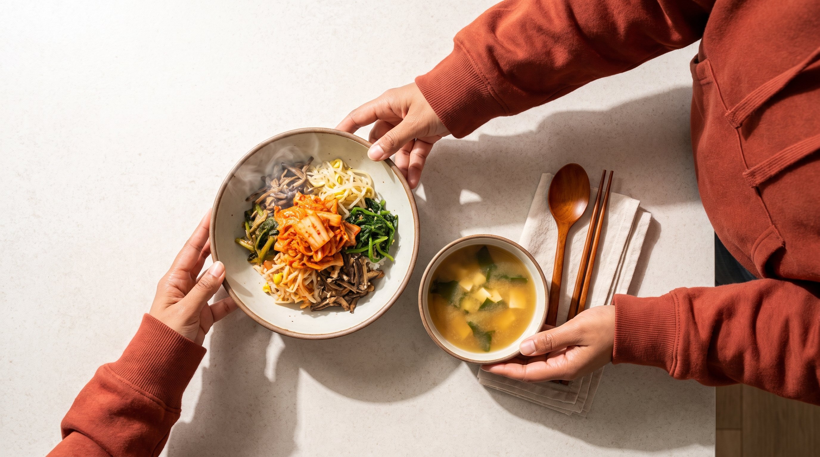 person spooning kimchi onto a bowl of rice at a kitchen table