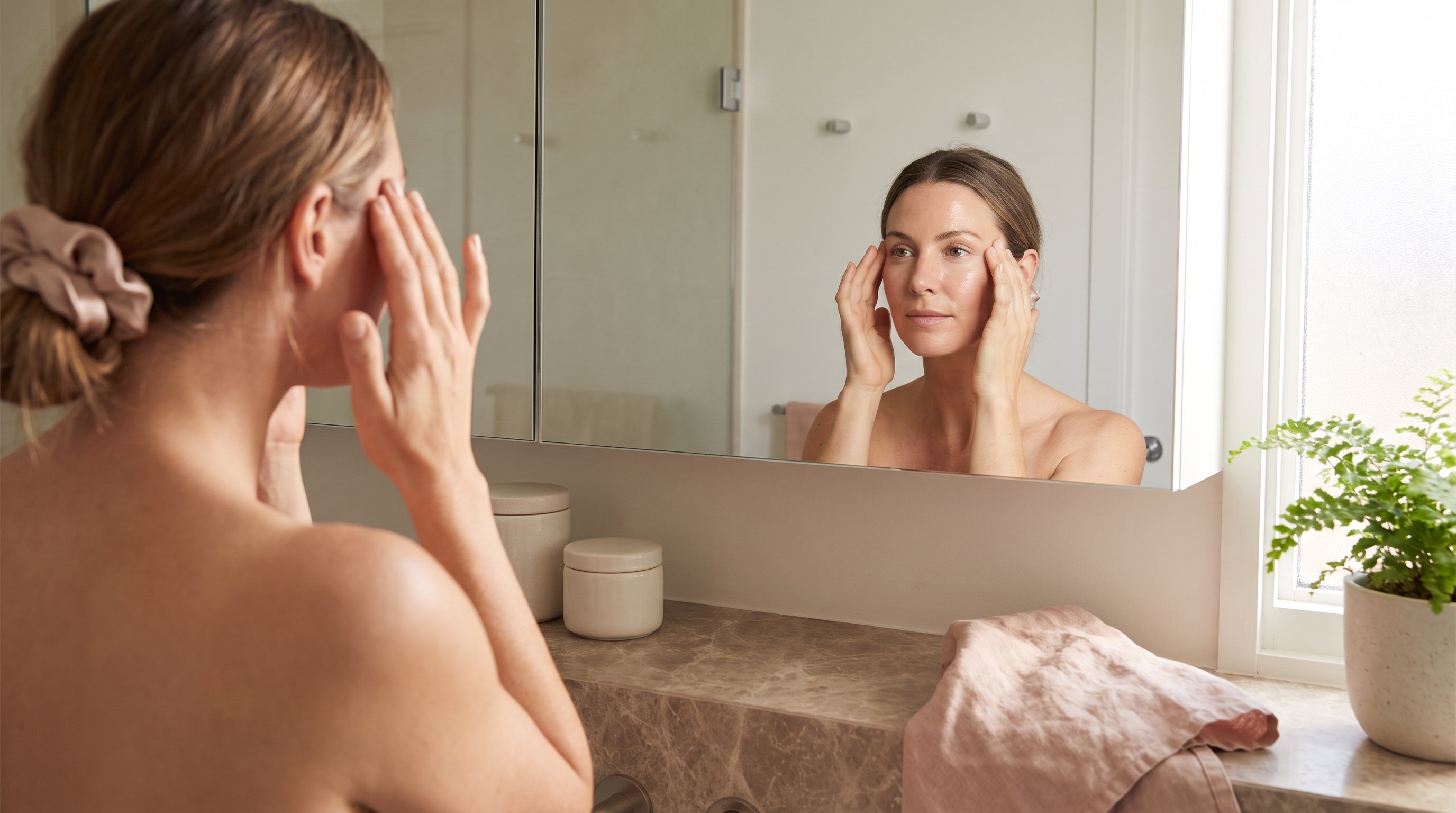 woman doing a face yoga exercise in front of a mirror