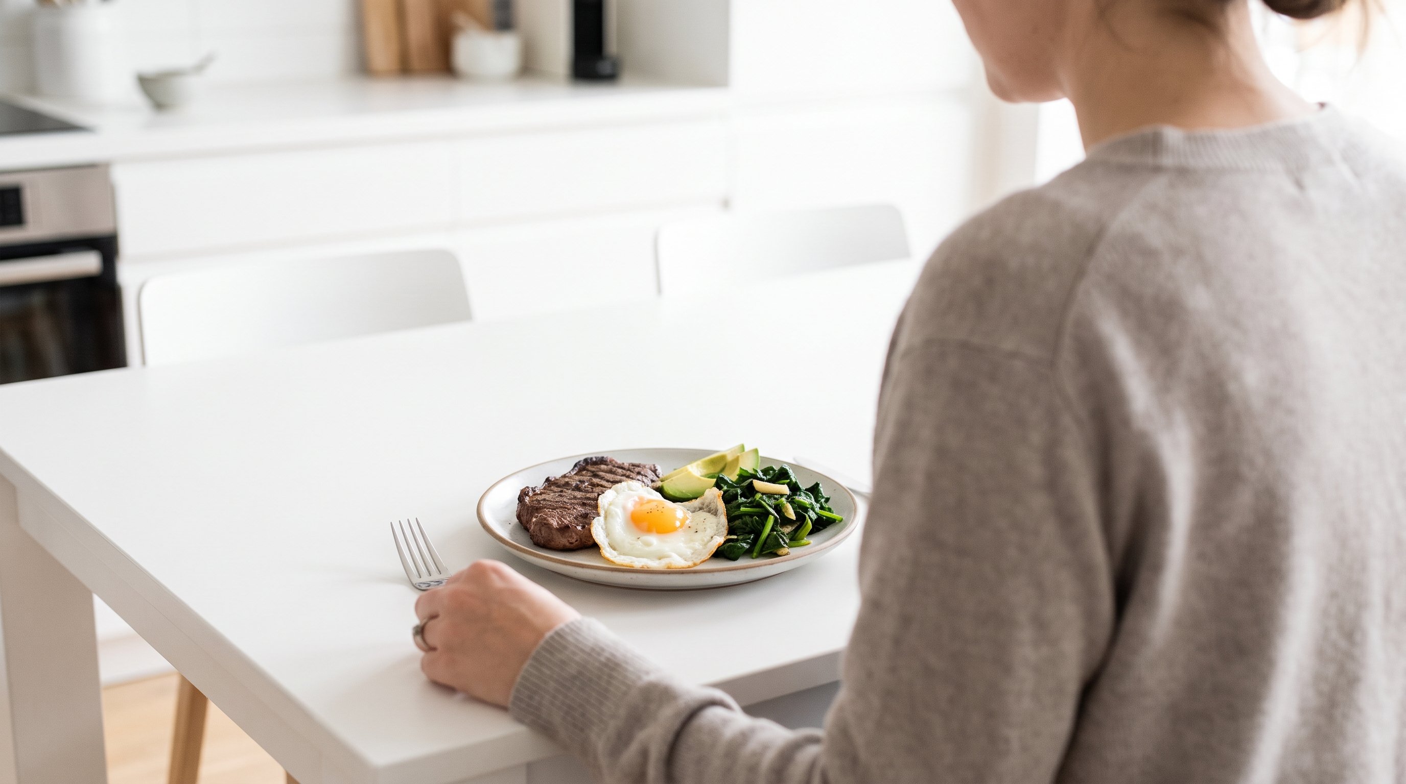 A plate of steak, eggs and greens ready to eat on a calm white dining table
