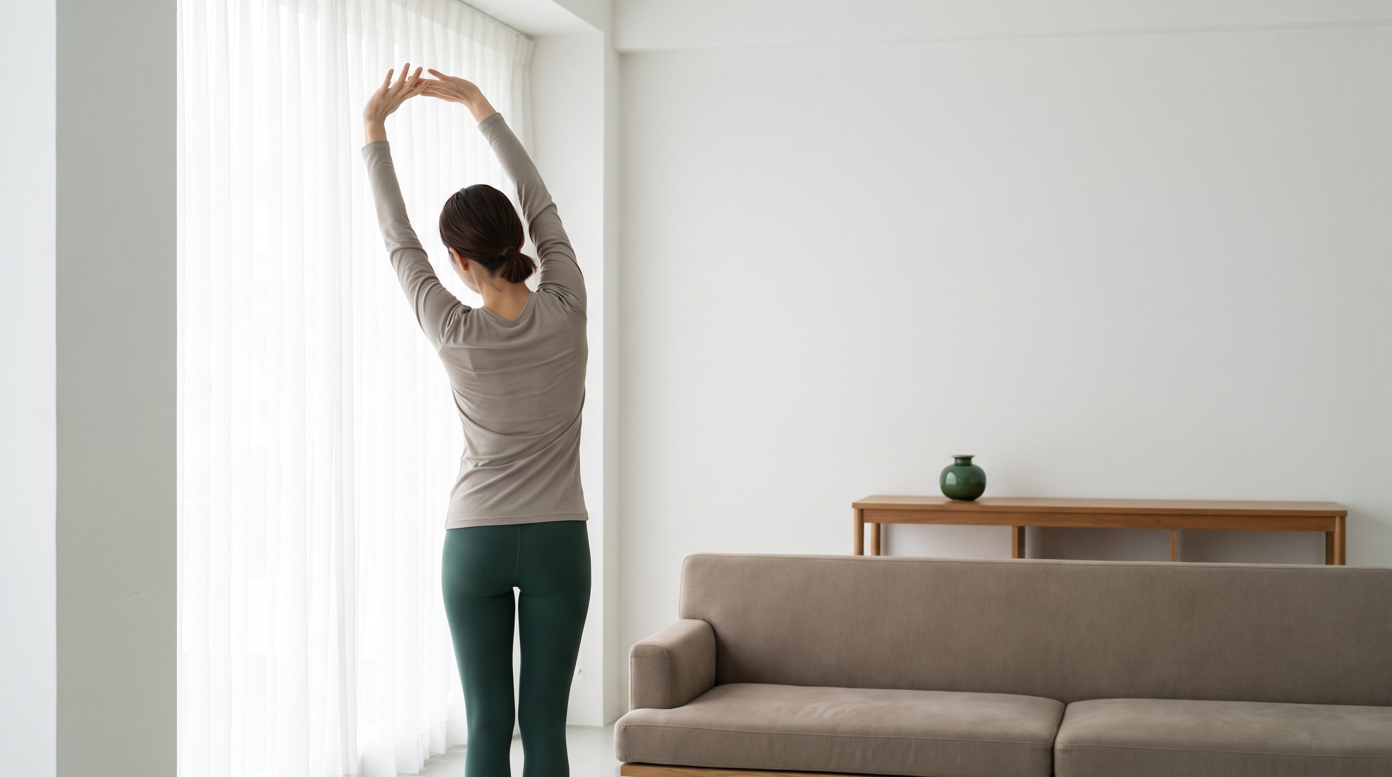 woman stretching arms overhead by a sunlit window