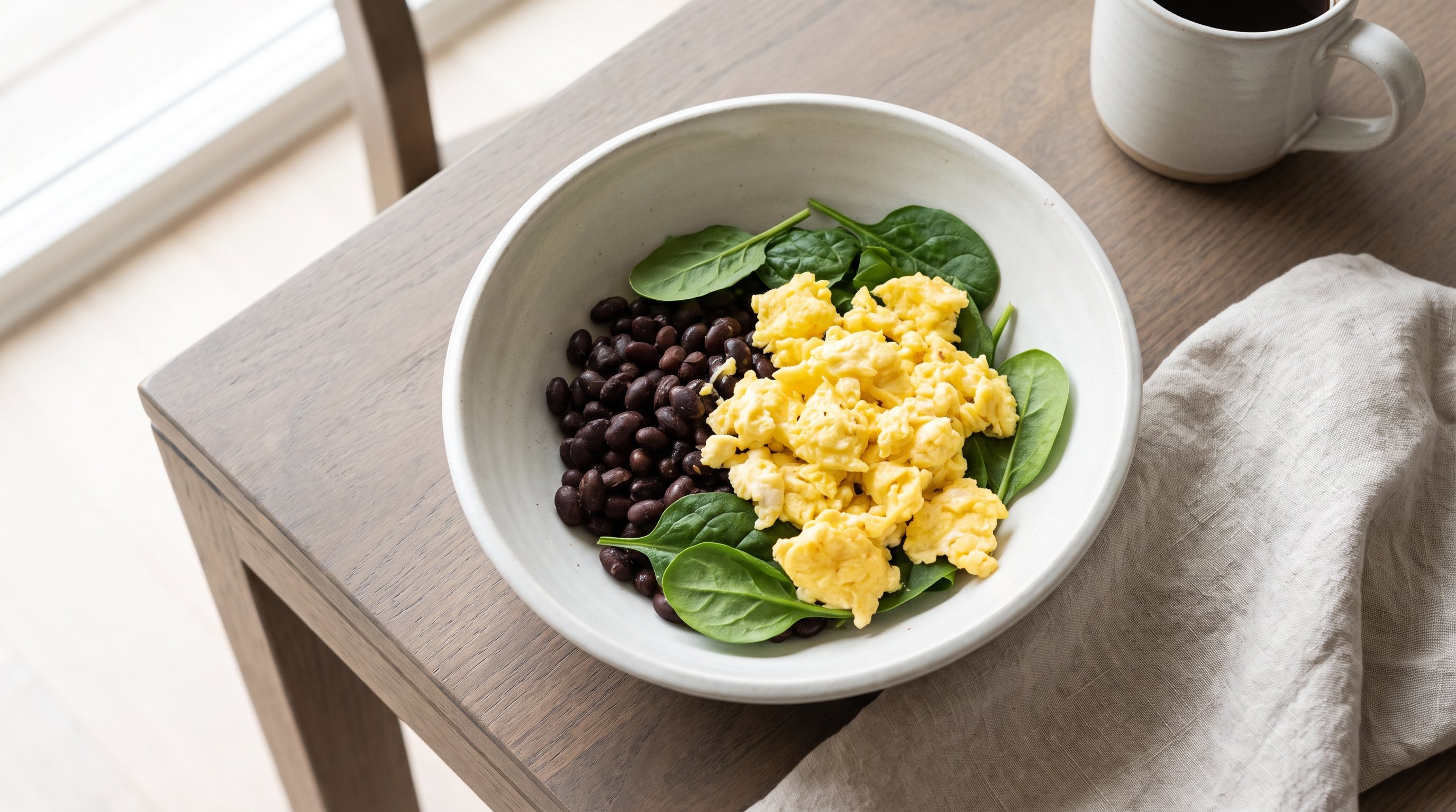bowl of scrambled eggs beans and spinach on a wooden table